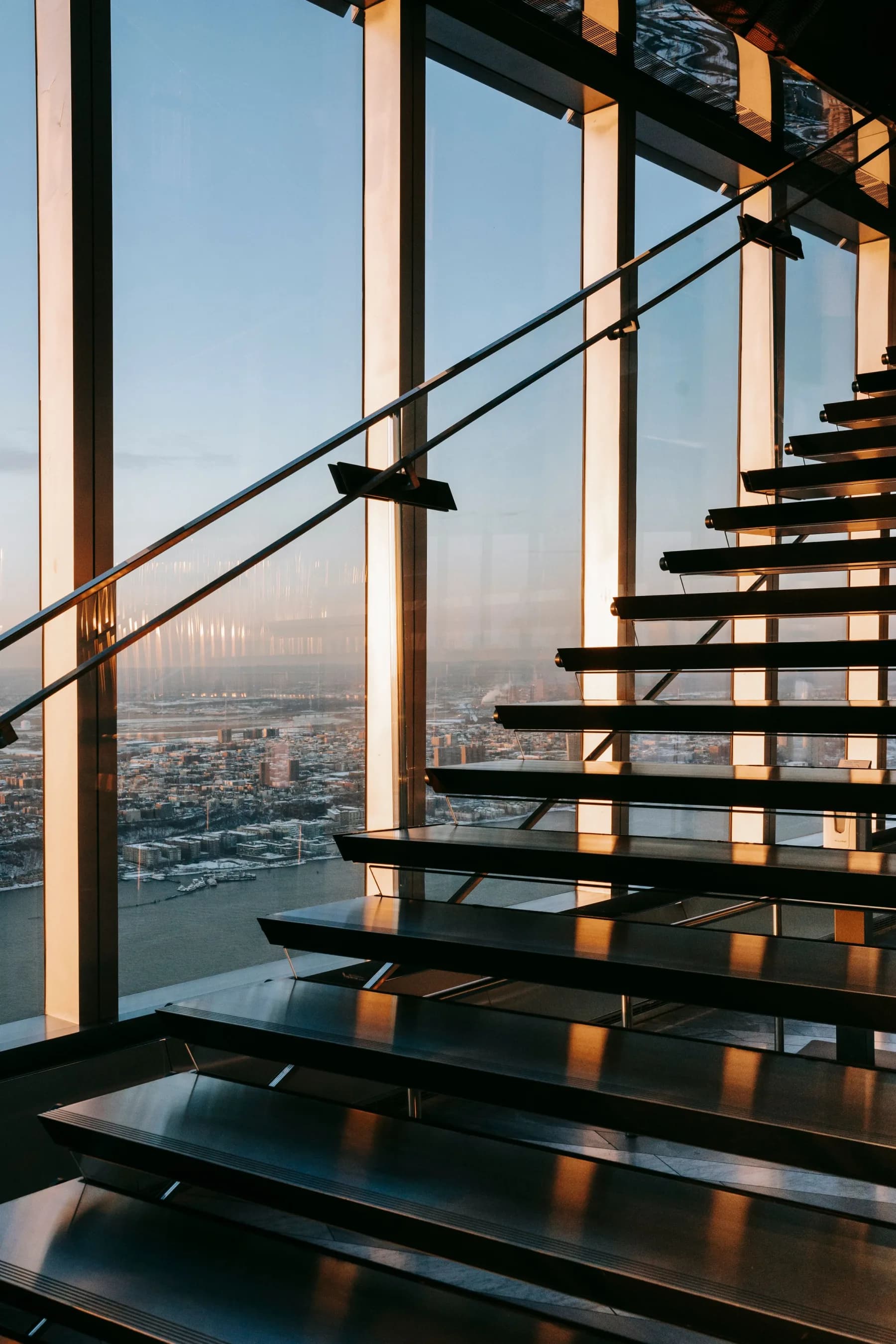 Escalera suspendida frente a una fachada de vidrio al atardecer